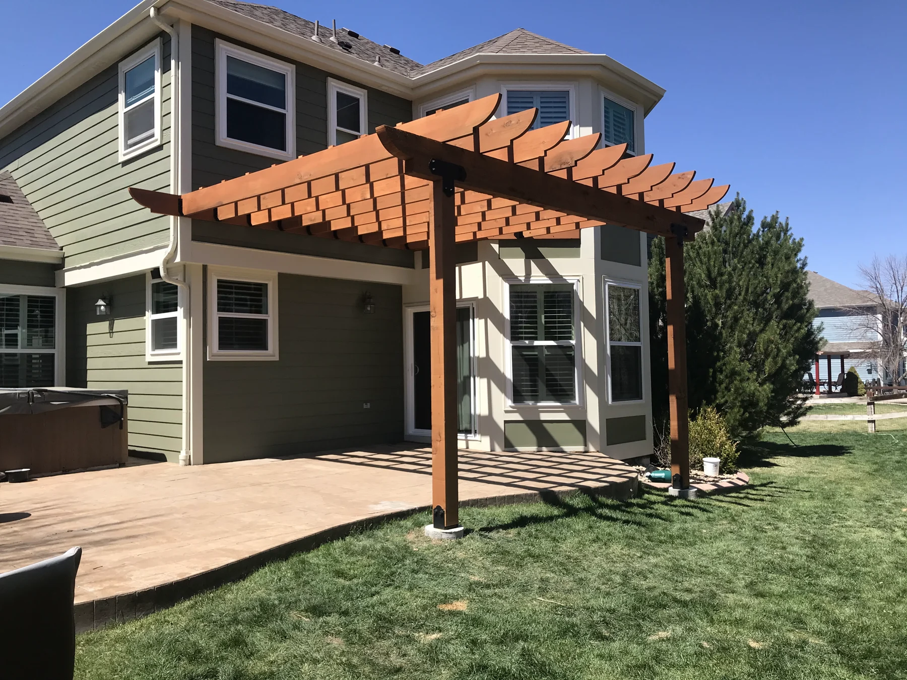 Colorado home with green lap siding, white window trim, and a timber pergola over the patio